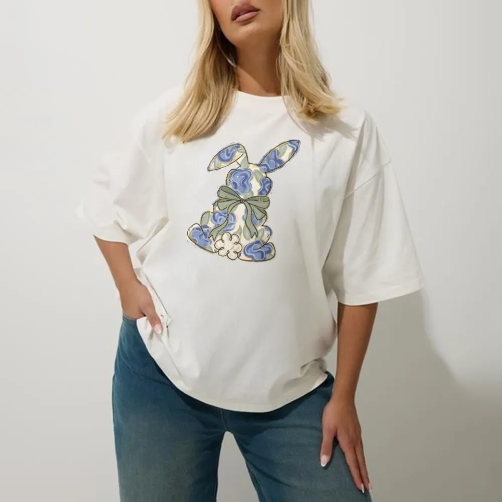 The Cartoon Rabbit Pattern Is Mainly Decorated With Blue And White Flowers And Tied With A Light Green Bow. The Style Is Fresh And Elegant, And It Is A Casual T-Shirt.
