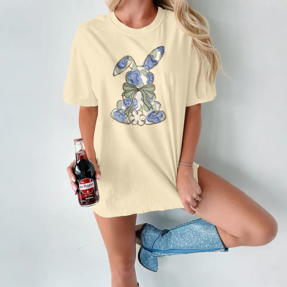 The Cartoon Rabbit Pattern Is Mainly Decorated With Blue And White Flowers And Tied With A Light Green Bow. The Style Is Fresh And Elegant, And It Is A Casual T-Shirt.