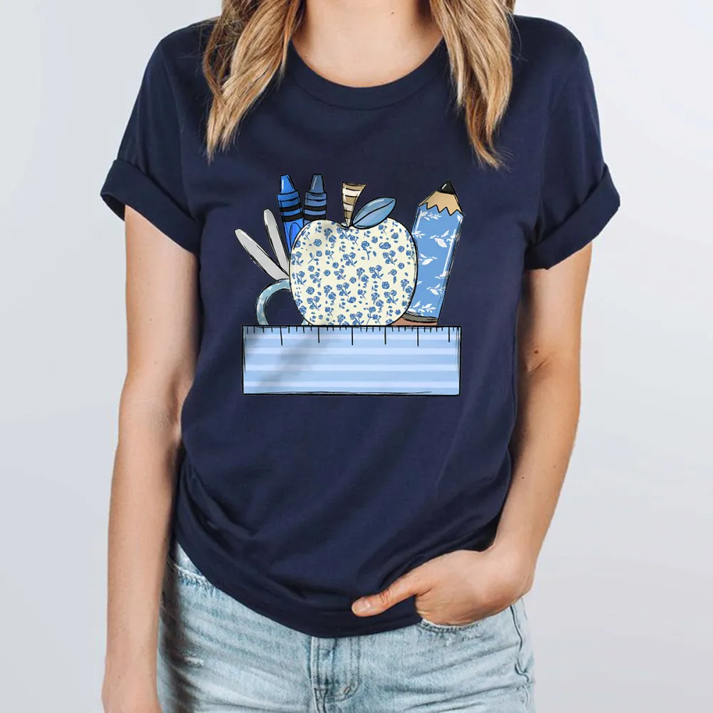An Apple With A Blue Flower Pattern Surrounded By Stationery, Including Blue Crayons, Pencils, Scissors And Paper Clips, And A Light Blue Ruler At The Bottom, With A Casual T-Shirt.