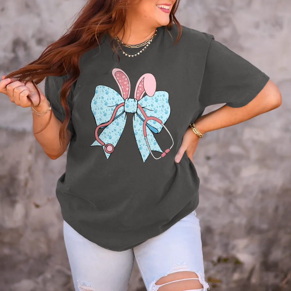 A Cartoon Rabbit Ear Element Bow Pattern, The Bow Has Blue Dots, The Rabbit Ears Are Pink With White Dots And A Pink Stethoscope Pattern, Casual T-Shirt