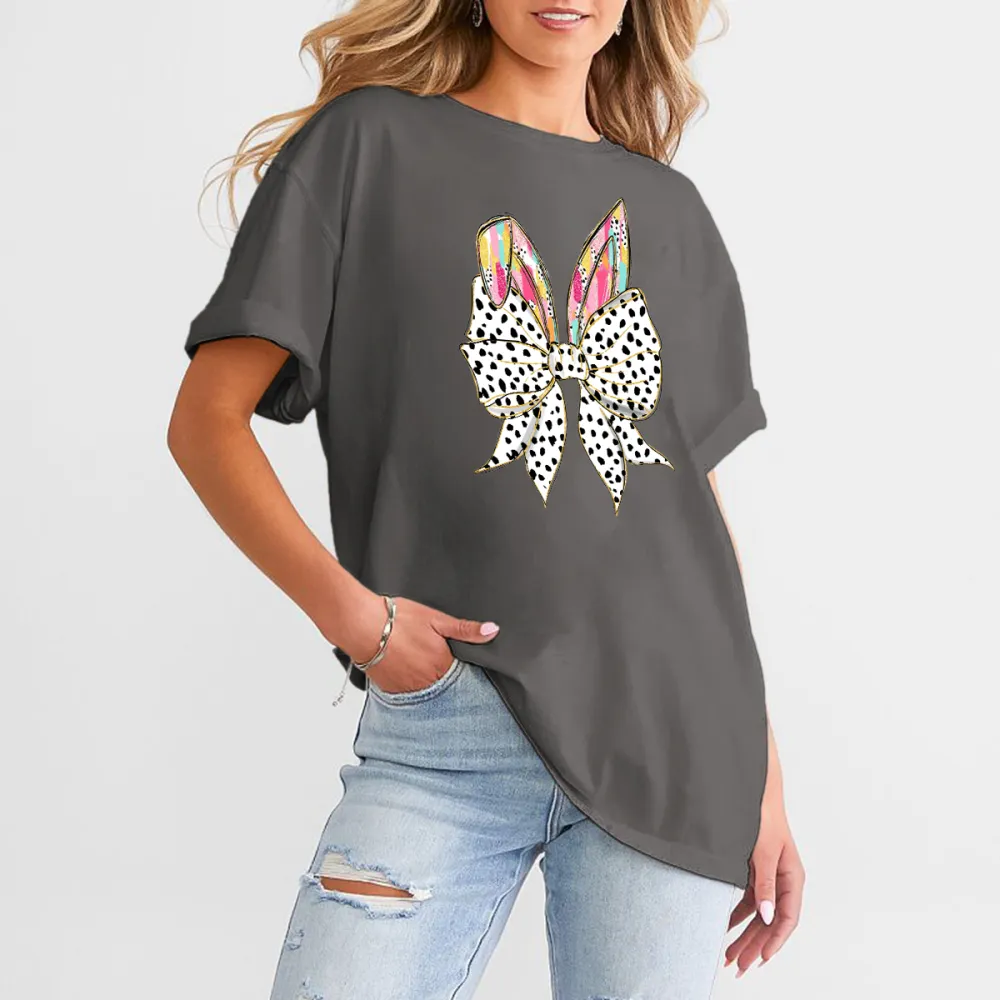 The Bow Is Made Of Black And White Polka Dots, The Bunny Ears Have Colorful Feather-Like Patterns, And The T-Shirt Is Casual.