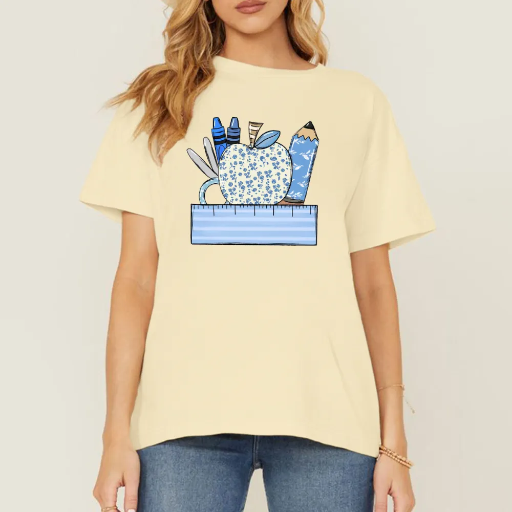 An Apple With A Blue Flower Pattern Surrounded By Stationery, Including Blue Crayons, Pencils, Scissors And Paper Clips, And A Light Blue Ruler At The Bottom, With A Casual T-Shirt.