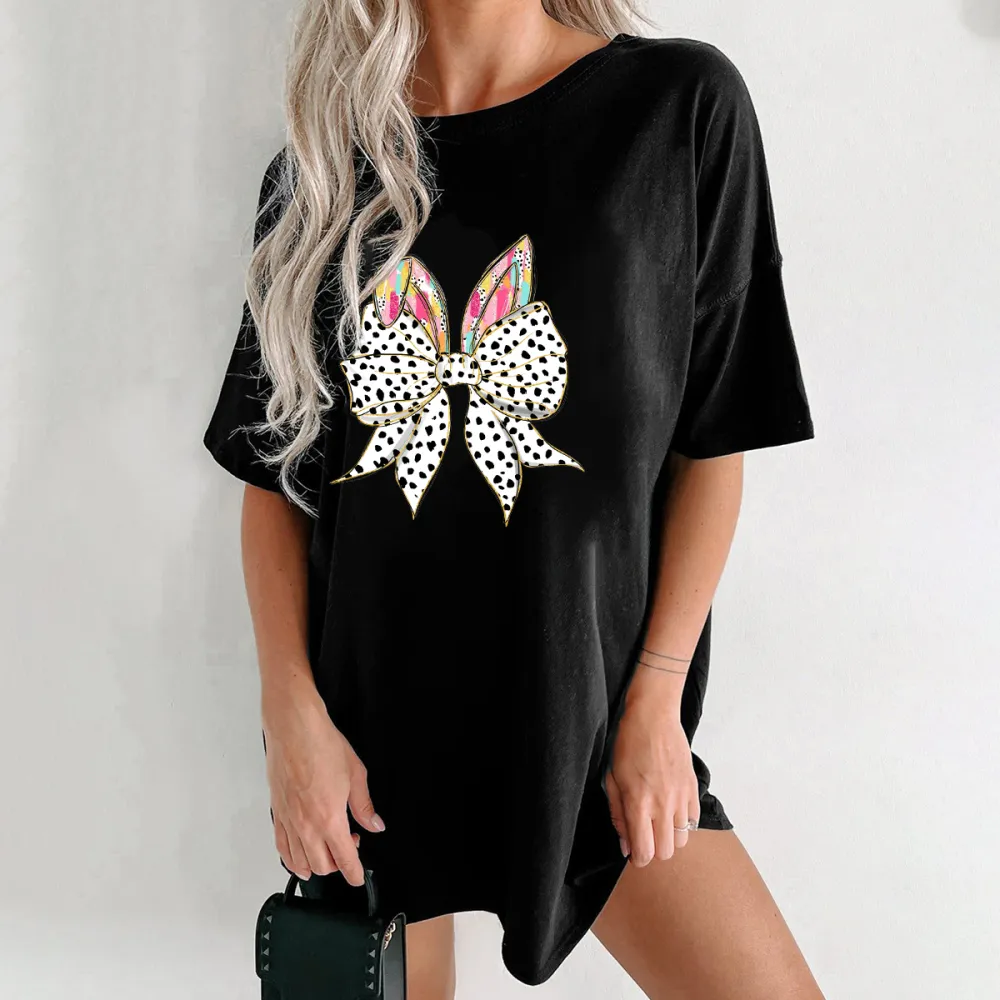 The Bow Is Made Of Black And White Polka Dots, The Bunny Ears Have Colorful Feather-Like Patterns, And The T-Shirt Is Casual.